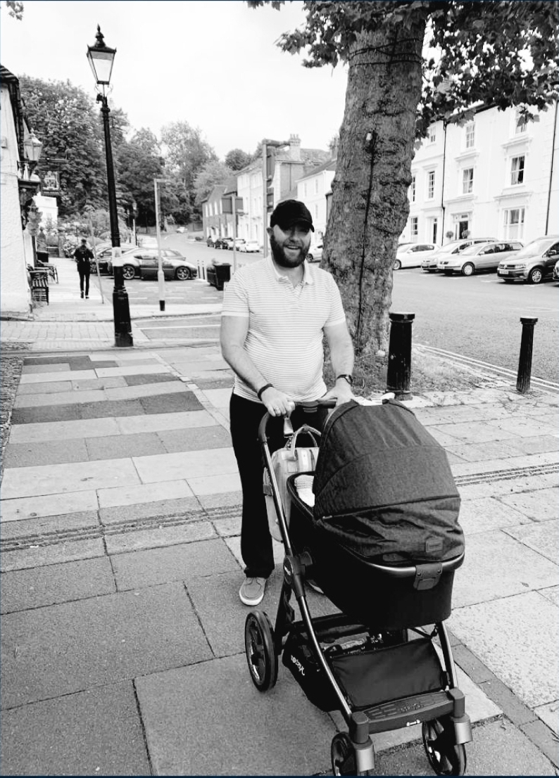 A new father pushing a pram on a quiet street.